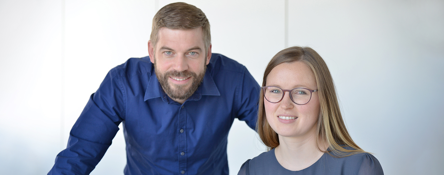 Ein Mitarbeiter und eine Mitarbeiterin von Testo arbeiten gemeinsam am Schreibtisch und blicken gemeinsam in die Kamera.